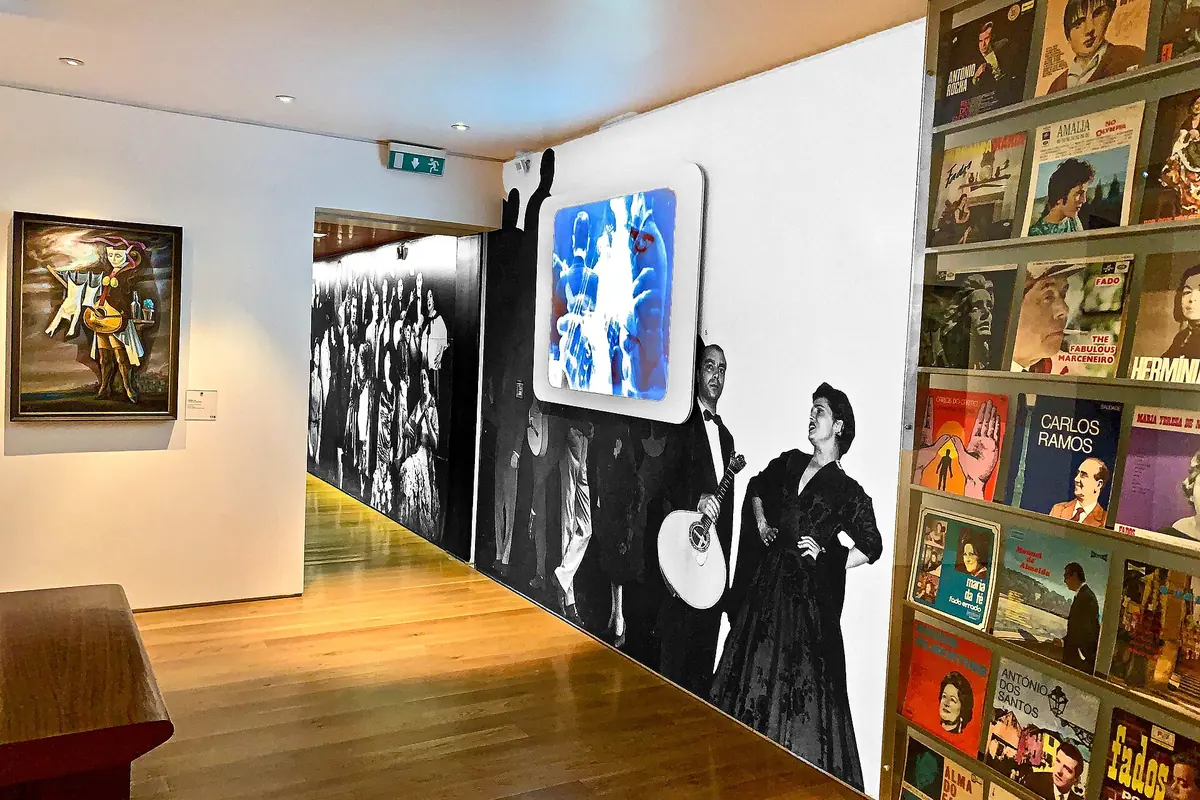 Um corredor do Museu do Fado com uma parede de capas antigas de discos de fado de um lado e uma grande fotografia de dois músicos de fado do outro