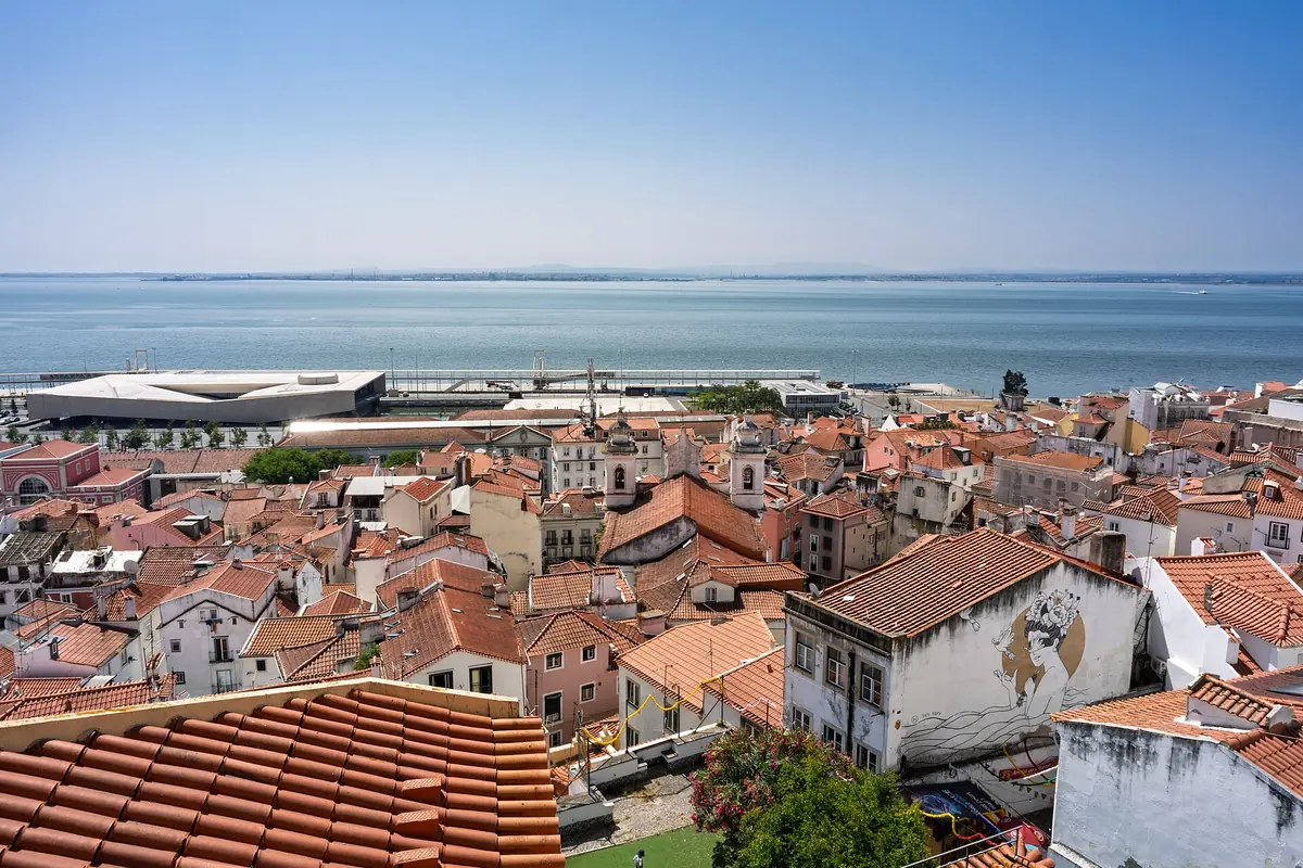 Široký výhled na červené taškové střechy Alfamy z vyhlídky Santa Luzia, za níž se rozprostírá řeka Tejo