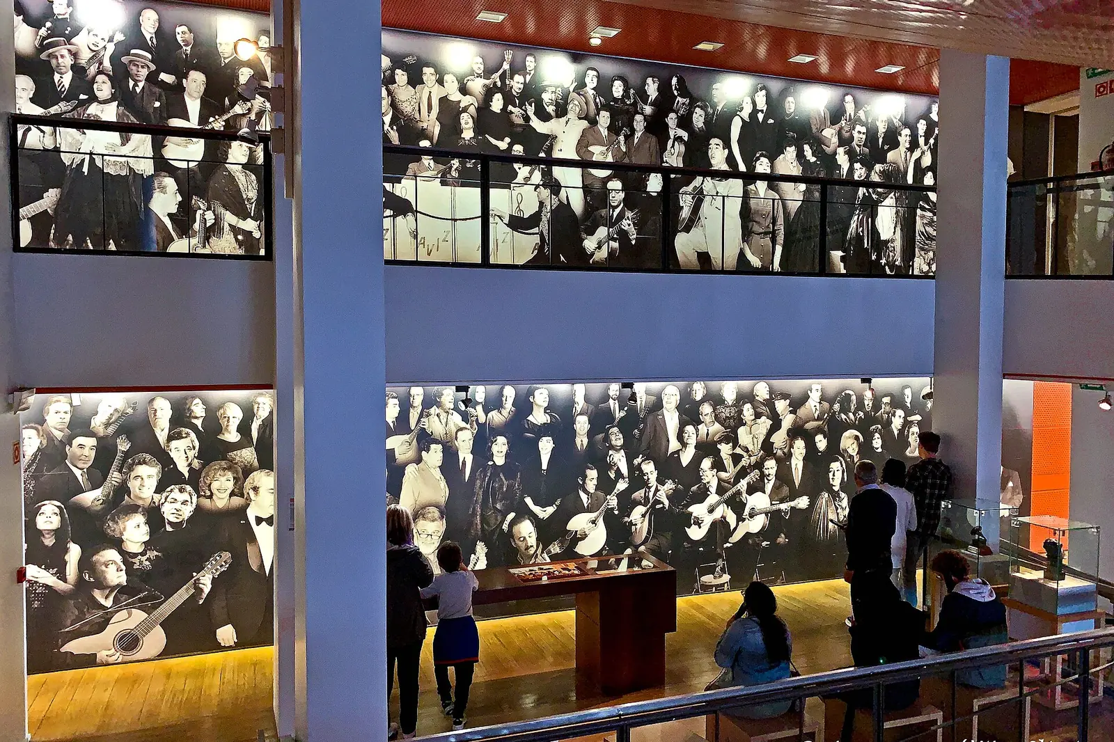 Eine Galerie im Museu do Fado in Lissabon mit einer hohen Wand aus Schwarz-Weiß-Fotografien von Fado-Publikum und Gitarristen